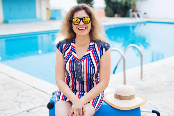 Meisje op zomervakantie op de achtergrond van zwembad, gekleed gestreepte jurk en zonnebril. — Stockfoto