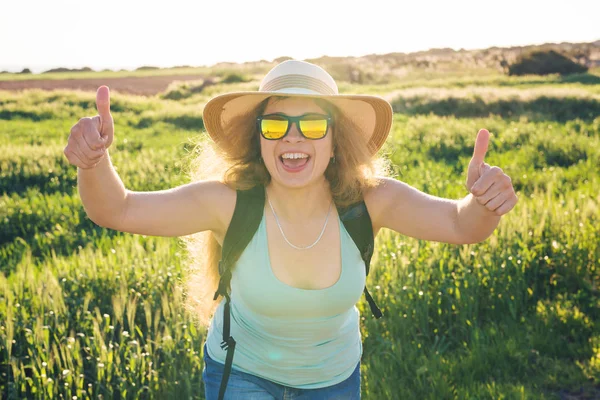 Zomer vakantie reizen en hitch wandel-concept - succesvolle gelukkige vrouw doen duimen omhoog gebaar op zomer velden achtergrond goed te keuren. — Stockfoto