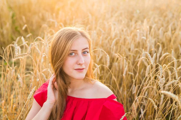 Retrato de una joven vestida de rojo sobre un fondo de campo de avena dorada, verano al aire libre . — Foto de Stock