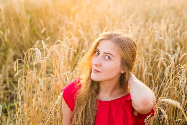 Portret van een jonge vrouw in rode jurk op een achtergrond van gouden haver veld, zomer buiten. — Stockfoto