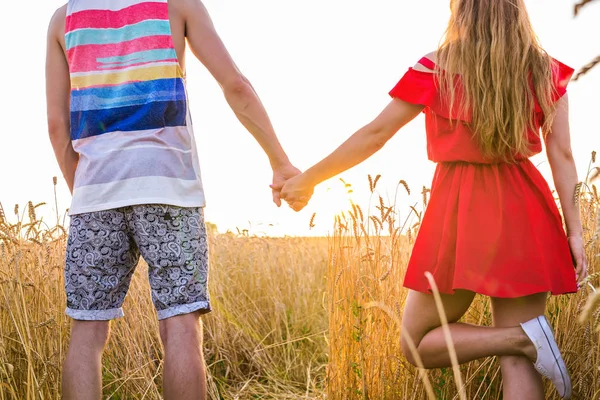 Mladý pár drží ruce v pšeničném poli v slunečný letní den — Stock fotografie
