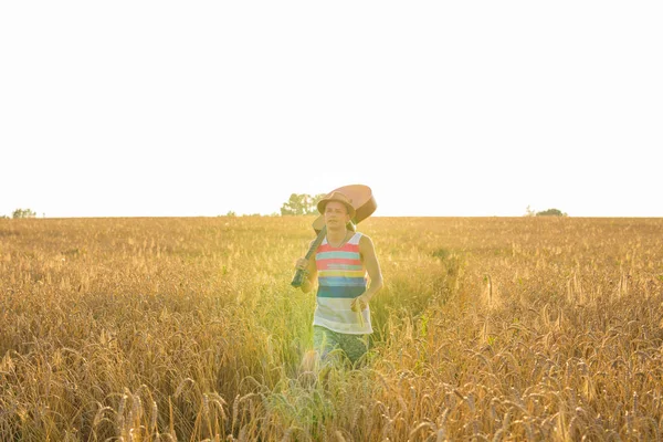 Músico sosteniendo guitarra acústica y caminando en campos de verano al atardecer . — Foto de Stock