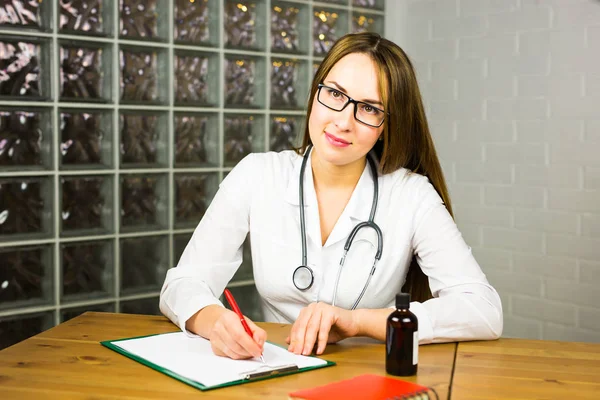 여성 의사 의학 의사 또는 약사 작업 테이블에 앉아, jar 또는 알 약의 병을 손에 들고, 특별 형식에 처방전을 쓰기. 의료, 약국 이나 건강 보험 — 스톡 사진