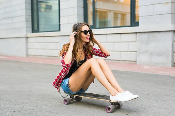 Junge Frau, die auf dem Skater sitzt. Lächelnde Frau mit Skateboard im Freien — Stockfoto