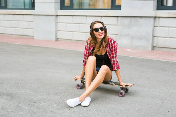 Uma jovem sentada no patinador. Mulher sorridente com skate ao ar livre — Fotografia de Stock