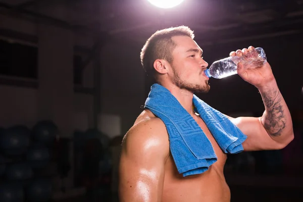young caucasian bodybuilder in the gym drinking a bottle water.