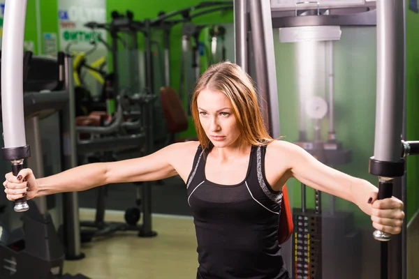 Jonge fitness vrouw uitvoeren oefening met oefening-machine in sportschool — Stockfoto