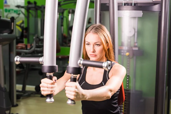 Jonge fitness vrouw uitvoeren oefening met oefening-machine in sportschool — Stockfoto