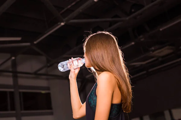 Mujer fitness bebiendo agua de la botella. Musculosa joven en el gimnasio tomando un descanso del entrenamiento . —  Fotos de Stock