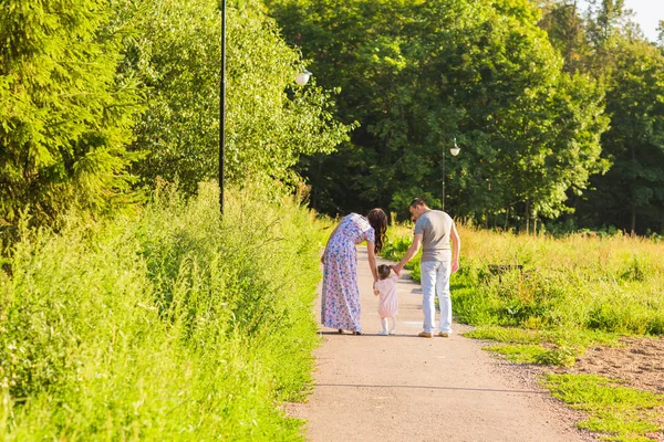 Concept de famille, de parentalité et de personnes - mère heureuse, père et petite fille marchant dans un parc d'été — Photo