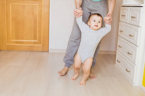 Bonito menino dando os primeiros passos segurando as mãos das mães . — Fotografia de Stock