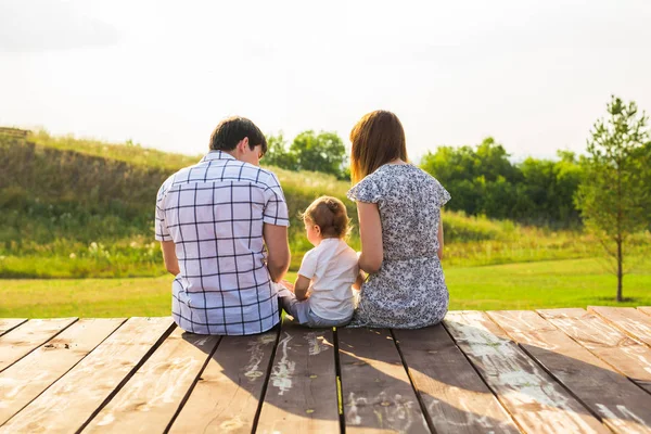 Vista trasera de la madre, el padre y el hijo sentados juntos al aire libre — Foto de Stock