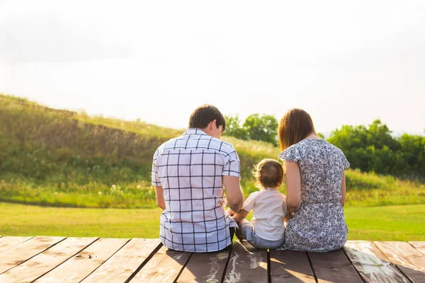 Rear view of mother, father and son sitting together outdoors — Stock Photo, Image