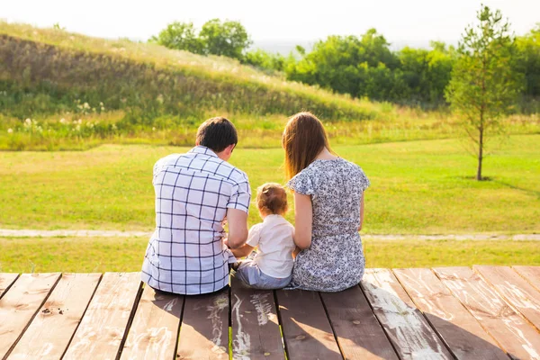 Vista trasera de la madre, el padre y el hijo sentados juntos al aire libre — Foto de Stock