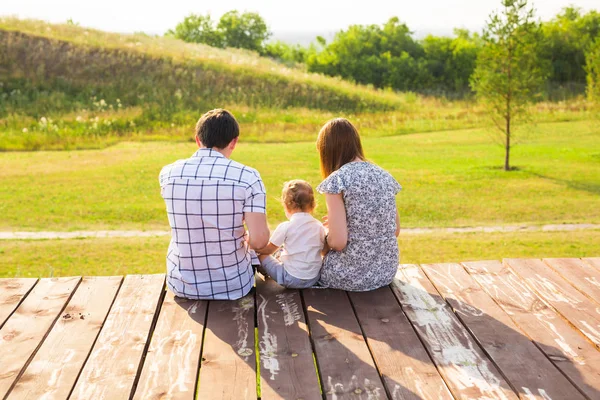 Rear view of mother, father and son sitting together outdoors — Stock Photo, Image