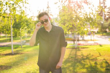 Yakışıklı şık hipster erkekte güzel manzarayı güneş doğa poz güneş gözlüğü