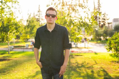 Yakışıklı şık hipster erkekte güzel manzarayı güneş doğa poz güneş gözlüğü