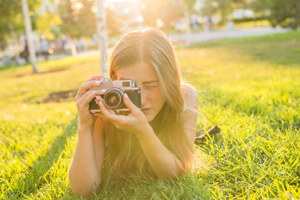 Krásná dívka fotograf drží kameru a ležet v trávě na jaře venku v parku. Koncepce cestovního ruchu a cestování. — Stock fotografie