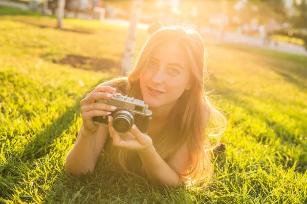 Krásná dívka fotograf drží kameru a ležet v trávě na jaře venku v parku. Koncepce cestovního ruchu a cestování. — Stock fotografie