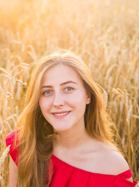 Retrato de una joven vestida de rojo sobre un fondo de campo de avena dorada, verano al aire libre — Foto de Stock