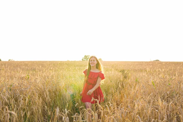 Mujer joven en vestido rojo caminando sobre un fondo de campo de avena dorada, verano al aire libre — Foto de Stock