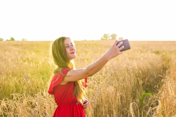 Mladá šťastná žena s úsměvem při pořizování selfie obrázek s mobilním telefonem v poli — Stock fotografie
