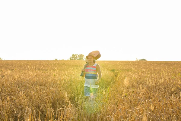 Músico sosteniendo guitarra acústica y caminando en campos de verano al atardecer —  Fotos de Stock