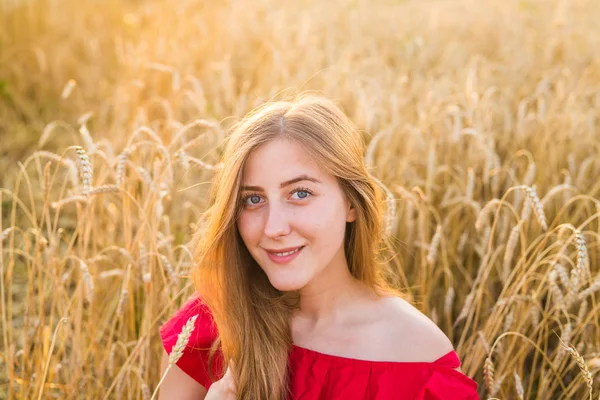 Retrato de una joven vestida de rojo sobre un fondo de campo de avena dorada, verano al aire libre — Foto de Stock