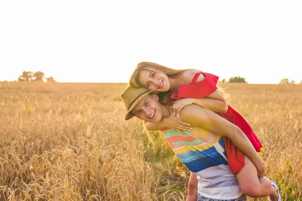 Casal feliz se divertindo ao ar livre no campo de trigo ao pôr do sol. Rindo Família alegre juntos. Conceito de Liberdade. Piggyback. . — Fotografia de Stock