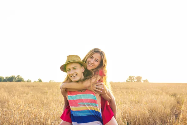 Casal feliz se divertindo ao ar livre no campo de trigo ao pôr do sol. Rindo Família alegre juntos. Conceito de Liberdade. Piggyback. . — Fotografia de Stock