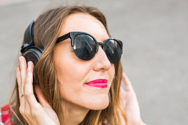 Young smiling woman relaxing and listening to music with headphones in the street