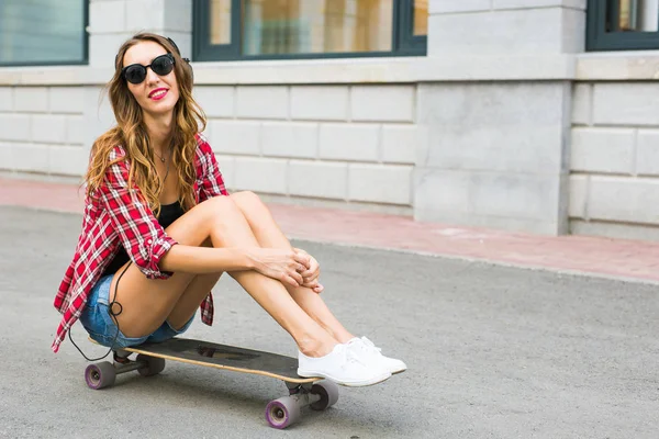 Mulher bonita em óculos de sol assento no skate, estilo de vida de rua moda . — Fotografia de Stock