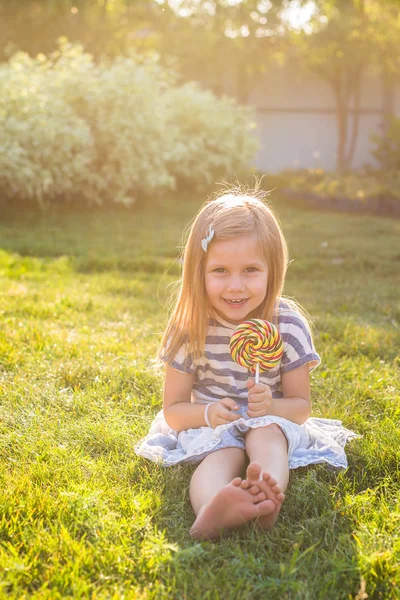 Roliga barn med candy lollipop, glad liten flicka äter stora socker lollipop, kid äta godis — Stockfoto