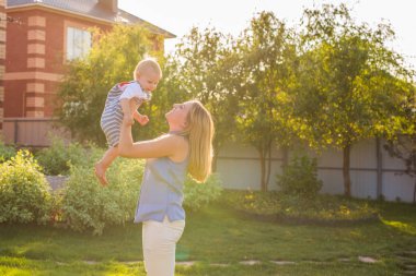 Açık havada mutlu ve uyumlu bir aile. Anne bebeği kusuyor, gülüyor ve yazın doğada oynuyor..