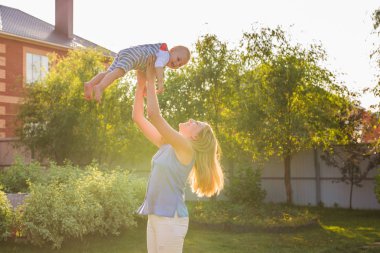 Açık havada mutlu ve uyumlu bir aile. Anne bebeği kusuyor, gülüyor ve yazın doğada oynuyor..