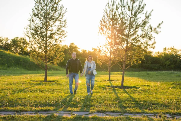 Mujer embarazada con marido caminando en el prado a la luz del sol — Foto de Stock