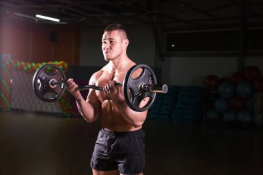 Spor salonunda halterle egzersiz yapan kaslı bir adam. Güçlü erkek, çıplak karın kasları..