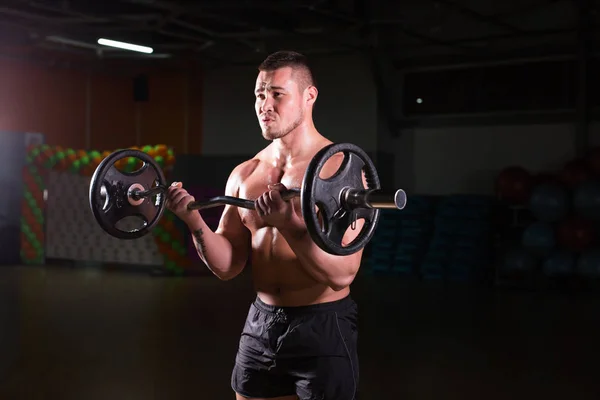 Sportlicher Mann macht Übungen mit Langhantel auf dunklem Hintergrund — Stockfoto