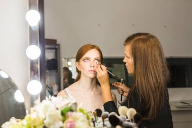 Makyaj yapma işlemi. Fırça ile çalışma modeli yüzünde makyaj sanatçısı. Güzellik Salonu iç genç Kızıl saçlı kadın portresi. Cilde uygulanan sesi.