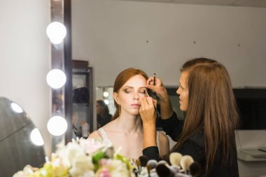 Makyaj yapma işlemi. Fırça ile çalışma modeli yüzünde makyaj sanatçısı. Güzellik Salonu iç genç Kızıl saçlı kadın portresi. Cilde uygulanan sesi.