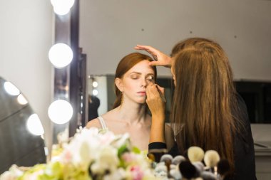 Makyaj yapma işlemi. Fırça ile çalışma modeli yüzünde makyaj sanatçısı. Güzellik Salonu iç genç Kızıl saçlı kadın portresi. Cilde uygulanan sesi.