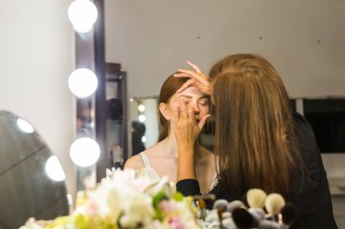 Makyaj yapma işlemi. Fırça ile çalışma modeli yüzünde makyaj sanatçısı. Güzellik Salonu iç genç Kızıl saçlı kadın portresi. Cilde uygulanan sesi.