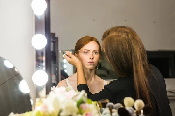 Maquillar artista haciendo profesional maquillaje de joven pelirroja mujer — Foto de Stock