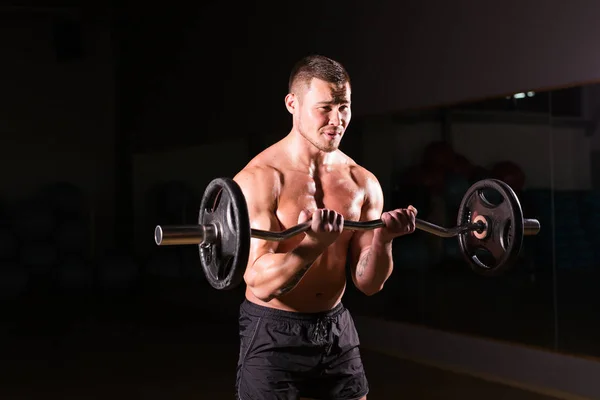 Muskulöser Mann trainiert im Fitnessstudio mit Langhantel, kräftigem nacktem Oberkörper. — Stockfoto
