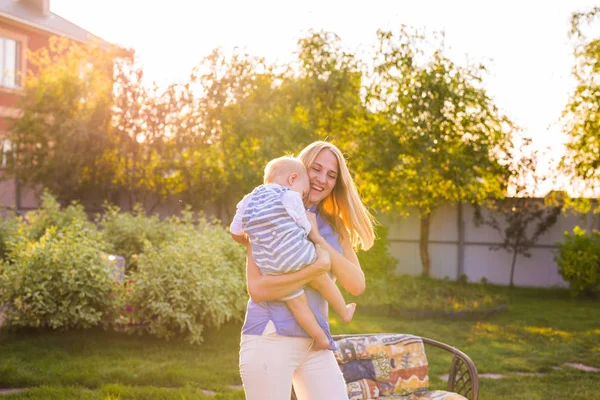 Lekfulla kvinnan i den trädgården spelar med hennes baby son — Stockfoto