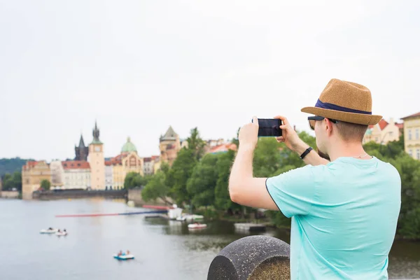 Vista trasera de un turista joven tomando fotos con teléfono inteligente frente al río y la ciudad — Foto de Stock