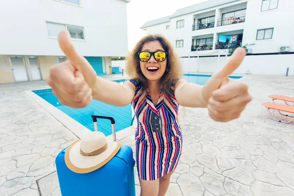Gelukkig meisje duimen opdagen op zomervakantie op de achtergrond van zwembad, gekleed gestreepte jurk en zonnebril. — Stockfoto