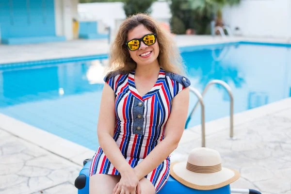 Portret van gelukkig meisje op zomervakantie op de achtergrond van zwembad, gekleed gestreepte jurk en zonnebril. — Stockfoto