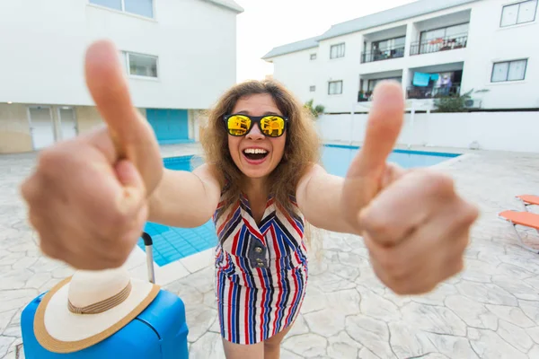 Gelukkig meisje duimen opdagen op zomervakantie op de achtergrond van zwembad, gekleed gestreepte jurk en zonnebril. — Stockfoto