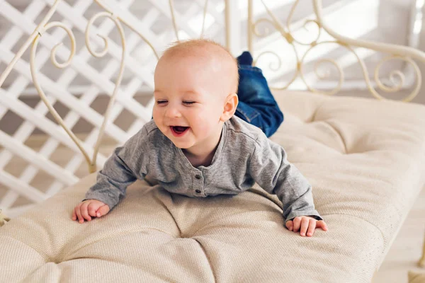 Adorable niño riendo en el dormitorio soleado. Niño recién nacido relajándose. Guardería infantil para niños pequeños.Mañana familiar en casa. Niñito acostado boca abajo —  Fotos de Stock